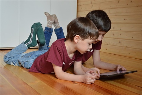 Two kidsplaying on a tablet.